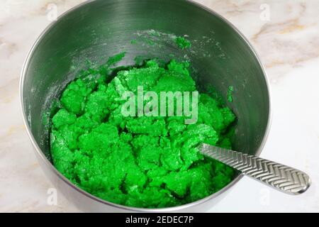 Teig für grüne St. Patrick`s Day Cookies durch Mischen Zutaten aus Mehl Butter Ei und grüne Lebensmittel Färbung Edelstahl Rührschüssel aus Stahl Stockfoto